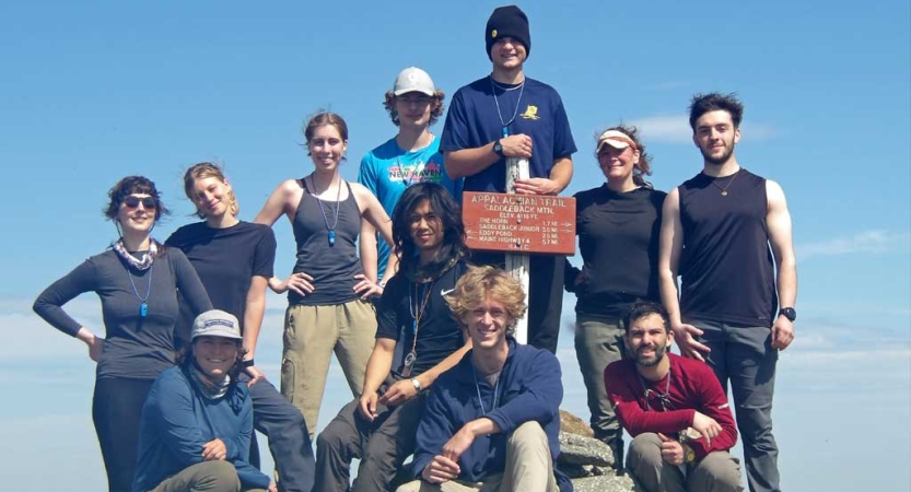 A group of people pose for a group photo on the summit of a mountain under a blue sky